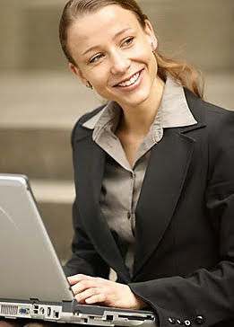 Smiling woman with blonde hair and a black blazer, typing on a laptop